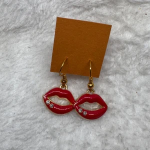 Röda läpp-örhängen med stenar - Coola örhängen i form av röda läppar med små glittriga stenar. Hängande modell med guldfärgade krokar. Perfekt accessoar för att sticka ut och ge din look en lekfull touch.