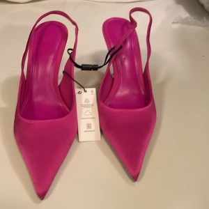 Rosa pumps med spetsig tå och klack - Snygga pumps från Zara i stark rosa färg med spetsig tå och smal klack. Skorna har öppen häl med smal rem och är tillverkade i satinliknande material som ger en lyxig känsla. Perfekta för dig som vill sticka ut med färg och stil. Ny pris 559 kr.