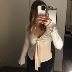 Vit långärmad topp med snörning  - Säljer en vit långärmad topp med v-ringning och knyt framtill. Toppen har utsvängda ärmslut och är figurnära i modellen. Perfekt för dig som gillar en stilren och trendig look.❤️knappt använd!