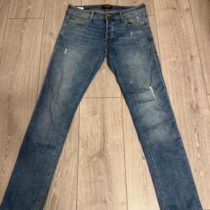 Jack & Jones Slim Glenn blå jeans - Snygga blå jeans från Jack & Jones, modell Slim Glenn. Jeansen har en slim passform, klassisk femficksdesign och lätt slitna detaljer framtill. Tillverkade i jeansmaterial med en bekväm känsla och snygg tvätt.