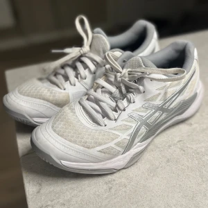 Vita Asics träningsskor/innebandyskor strl 38 - Säljer ett par fräscha vita Asics träningsskor (tex innebandy) i storlek 38. Skorna har grå detaljer, snörning och en sportig mesh- och syntetöverdel. Perfekta för dig som gillar stilrena och bekväma skor med riktigt bra grepp i sulan. Köpte tyvärr för liten storlek. Använda vid några tillfällen 