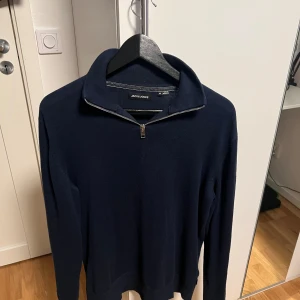 Mörkblå half zip tröja Jack & Jones - Mörkblå långärmad tröja från Jack & Jones med stilren half zip-dragkedja vid kragen. Tröjan är i mjukt stickat material och har en klassisk passform som funkar till många olika outfits. Perfekt för dig som gillar enkel och snygg stil. Storlek M! Tröjan är i mycket bra skick och inga defekter eller sådant!