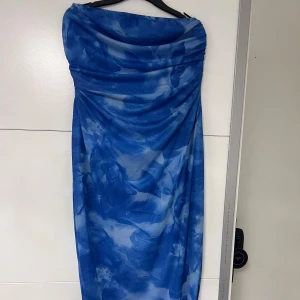 Blå långklänning med slits - Snygg axelbandslös långklänning i blått med mönstrad mesh och draperad överdel. Klänningen slits på sidan