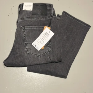 Grå jeans från Jack & Jones Glenn - Snygga grå jeans från Jack & Jones med klassisk femficksdesign och raka ben. Jeansen har en stilren look och är tillverkade i bomull med en mjuk känsla. Perfekta för dig som gillar en enkel och clean stil.