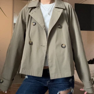 Beige skepparkavaj med knappar - Säljer en olivgrön trenchcoat med dubbelknäppning och stora bruna knappar. Jackan har en croppad passform och är i fint skick! Skriv vid funderingar💗