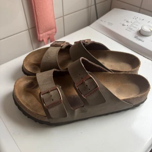 Bruna Birkenstock - Klassiska Birkenstock sandaler i brun skinn. Använda under en sommar så lite slitage men inte alldeles för mycket.