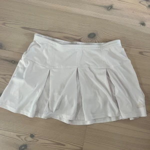 Vit padelkjol från Adidas - Vit padelkjol från Adidas med plisserade detaljer och undershorts. Kjolen är i storlek 38 men passar en storlek 36