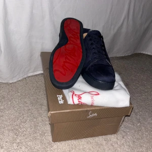 Mörkblå sneakers från Christian Louboutin - Snygga mörkblå sneakers från Christian Louboutin i mjuk mocka med klassisk röd sula och broderad logga på hälen. Skorna har rund tå, platt sula och snörning framtill. Perfekt för dig som vill sticka ut med exklusiv stil och detaljer.