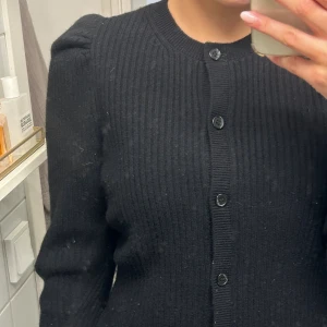Svart ribbad kofta från & Other Stories - Säljer en svart ribbstickad ull kofta från & Other Stories . Koftan har puffade axlar, rund halsringning och knäppning framtill med svarta knappar. Knappt använd så är i superform skick, skulle säga att den passar S och M 💞