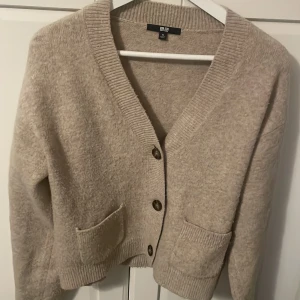 Beige kofta från Uniqlo XS - Mysig beige kofta från Uniqlo i storlek XS. Koftan har v-ringning, stora knappar framtill och två praktiska fickor. Den är stickad och har ribbade muddar vid ärmslut och nederkant. Perfekt för lager-på-lager under kyliga dagar. Ny pris 449kr! Perfekt nj till hösten 🍁🍁