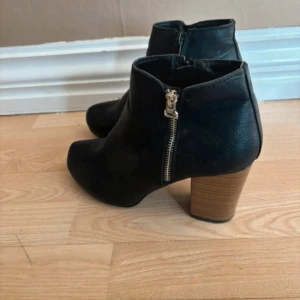 Svarta stövletter med klack och dragkedja - Snygga svarta stövletter med rund tå och grov träfärgad klack. Skorna har dragkedja på sidan som detalj och är tillverkade i skinnimitation. Liten nötning baktill. 