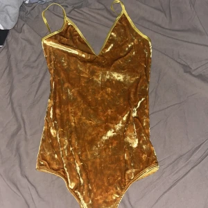 Guldig sammetsbody från Bik Bok - Supersnygg guldig body i sammet från Bik Bok med smala axelband och v-ringning. Perfekt för dig som vill sticka ut med en glansig och lyxig look. Säljs med prislapp kvar!