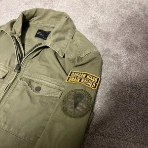 Olivgrön overshirt från Zara Man S - Olivgrön overshirt från Zara Man med dragkedja framtill, två bröstfickor och coola patches på ena ärmen. Jackan är i bomull och har en avslappnad passform som passar perfekt till jeans. Snygg militärinspirerad look.
