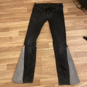 Lee svarta bootcut jeans W28 L32 - Svarta jeans från Lee i modellen Malone med bootcut och gråa paneler längst ner på benen. Tillverkade i ekologisk bomull. Snygg kontrast mellan svart och grått, klassisk femficksmodell och knappgylf. Perfekta för dig som vill sticka ut lite extra. Extremt lågmidjade 