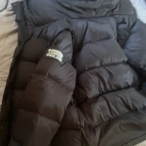 Svart pufferjacka från Burberry - Säljer en svart pufferjacka från Burberry London England. Jackan har klassisk Burberry-rutig insida i grå toner och är vadderad för extra värme. Stängs med dragkedja och har en oversized look. Perfekt för kalla dagar och riktigt snygg streetstil. Du kan även ta den som en väst alltså ta bort armarna för er som inte vet.