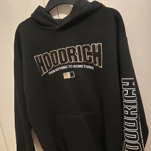Svart hoodie från Hoodrich med tryck - Svart hoodie från Hoodrich med stora tryck både fram och bak samt på ena ärmen. Snyggt broderad logga och texten 'From nothing to something'. Klassisk känguruficka och huva. Perfekt streetwear-vibe med coola detaljer i vitt och guld.