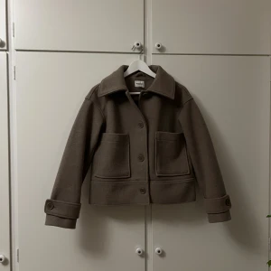 Brun/beige kort kappa med stora fickor - Brun/beige kappa från Kappahl  med stora framfickor, bred krage och knappar framtill. Den är i storlek XS men sitter som en S.  Hör av dig för fler bilder💕🌟