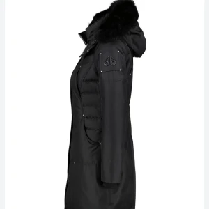 Svart lång dunjacka från Moose Knuckles - Snygg svart lång dunjacka från Moose Knuckles med avtagbar huva och fluffig pälsdetalj. Kvittot medföljer.