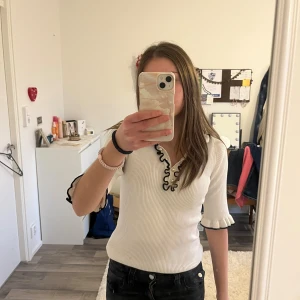 Vit ribbad topp med volang från Holly White - Supersöt vit ribbad topp från Lindex  med volangkant och svarta detaljer längs krage och ärmslut. Tröjan har dock en liten fläck men går nog enkelt att få bort! Pris kan diskuteras 