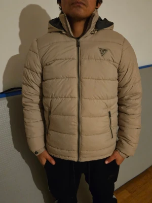 GUESS Beige jacka - Snygg beige dunjacka från Guess med quiltad design och huva. Den är använd någon gång bara. Ser ut som ny.
