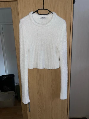 Vit stickad tröja från NA-KD - Mysig vit stickad tröja från NA-KD med ribbad struktur och croppad passform. Tröjan har långa ärmar och rund halsringning. Jag har vanligtvis XL i liknande tröjor med stor byst, den här tröjan är kort och slutar precis under mina bröst. Så jag skulle säga att den passar för dig med lite mindre byst. 