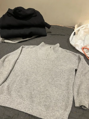 Ljusgrå stickad tröja med halvzip passar i xs och s - Ljusgrå stickad tröja med hög krage och halvzip framtill. Tröjan har en rak passform och ribbstickad struktur, vilket ger en avslappnad men ändå stilren look. Perfekt att bära över en t-shirt eller skjorta för extra lager.