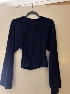 Mörkblå långärmad croppad topp - En stilren mörkblå långärmad topp med croppad passform och vida ärmar. Enkel design utan synliga detaljer eller mönster. Fint skick. 