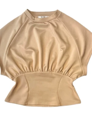 Beige topp från NA-KD med markerad midja - Trendig beige topp från NA-KD med korta ärmar och markerad midja. Toppen har en unik siluett med rynkade detaljer vid midjan och en mjuk, stretchig känsla. Perfekt att styla med både jeans och kjol för en cool look.