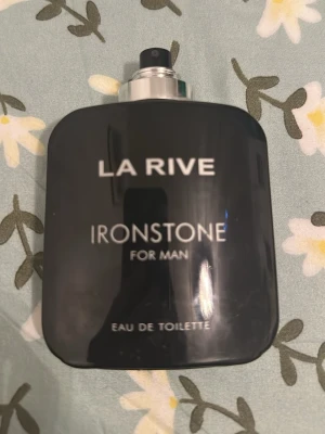 La Rive Ironstone Eau de Toilette - La Rive Ironstone Eau de Toilette för män kommer i en stilren, svart rektangulär flaska med silverfärgad spraykork. Doften är maskulin och flaskan har en modern design med tydlig logotyp och text i vitt.