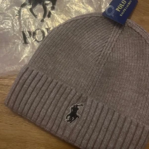 Beige ribbstickad mössa Polo Ralph Lauren - Snygg beige ribbstickad mössa från Polo Ralph Lauren med klassisk broderad logga framtill. Mössan har vikt kant och är tillverkad i mjukt material som håller dig varm. Perfekt accessoar för kalla dagar och enkel att matcha med olika outfits.