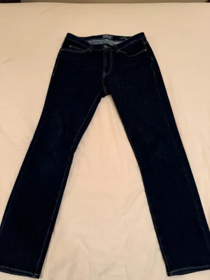 Dressmann Jeans Slim - Säljer ett par mörkblå jeans med slim passform och klassiska kontrastsömmar. Jeansen har fem fickor och bälteshällor, perfekta till en avslappnad stil. Materialet är bomull vilket gör dem bekväma att bära hela dagen.