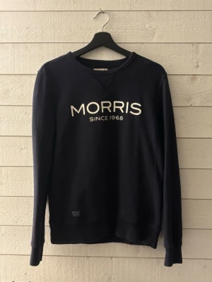 Mörkblå sweatshirt från Morris - Mörkblå sweatshirt från Morris med vit text 'MORRIS SINCE 1968' på bröstet. Tröjan har rund halsringning, långa ärmar och ribbade muddar vid ärmslut och nederkant. Perfekt för en avslappnad och stilren look.