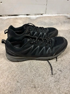 Svarta sneakers från Sprayway - Snygga svarta sneakers från Sprayway med mörkgrå detaljer och snörning. Ovandelen är i mesh och syntet för bra andningsförmåga och komfort. Platt sula och rund tå gör dem perfekta för träning eller vardagsaktiviteter. Klassisk och sportig design.