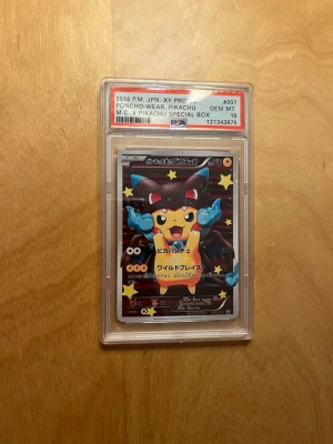 Pokémonkort Pikachu Poncho PSA 10 - Japanskt Pokémonkort från 2016 med Pikachu i Mega Charizard X-poncho, graderat PSA 10. Kortet har färgstark design med svart, blått och gult motiv och stjärnor i bakgrunden. Kortet är inneslutet i en genomskinlig PSA-plastbehållare. (Ej äkta). QR kod finns. 