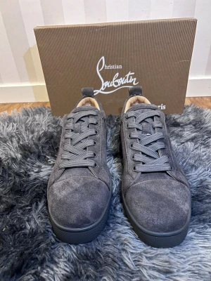 Christian Louboutin skor  - Snygga gråa sneakers från Christian Louboutin i mocka med klassisk röd sula. Skorna har rund tå, snörning och en stilren design som passar perfekt till streetwear. Insidan är ljusbeige och sulan är i gummi.