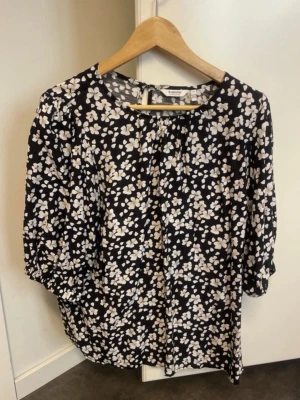 Svart blommig blus från KappAhl - Snygg svart blus från KappAhl med vitt blommönster. Blusen har rund halsringning och trekvartsärm med lätt puff och resår vid ärmslut. Luftig och skön passform, perfekt till jeans eller kjol. Materialet känns lätt och följsamt.