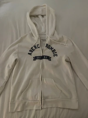 Vit hoodie från Abercrombie - En huvtröja från abercombie and fitch. Den har tyvärr några fläckar som jag inte lyckats få bort. Det är kanske möjligt men risken finns att de ej går att ta bort. Annars fint skick. Pris kan absolut diskuteras