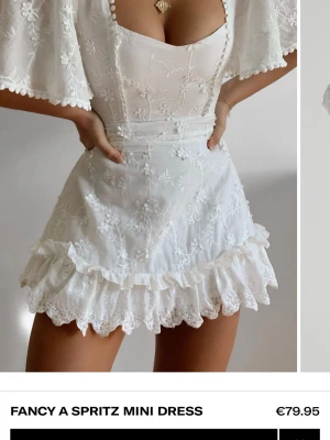 Vit klänning showpo - Supersöt vit kort klänning med broderade blommor, volangkant och fin skurning upptill.. Klänningen har vida korta ärmar och omlottkänsla upptill. Perfekt för sommarens alla tillfällen eller studenten!! Helt oanvänd, med alla lappar på eftersom den var för stor för mig. Storlek 38 men skulle säga att det är som 36/S💞💞