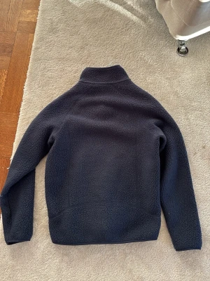 Mörkblå fleecejacka från Patagonia - mörkblå fleecejacka från Patagonia med hel dragkedja och tre fickor med blå detaljer. Har inte använt tröjan särskilt mycket, pga att jag växte och den blev för liten inom bara några månader.