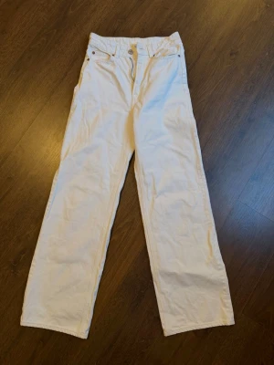 Vita raka jeans med bred passform - Säljer ett par vita/krämiga jeans med rak och bred passform. Jeansen har klassisk femficksdesign och stängs med knapp och dragkedja. Perfekta för dig som gillar en avslappnad och trendig look.