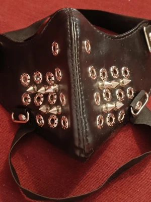 Gothic ansiktsmask med nitar och spikes - Cool svart mask i konstläder med silverfärgade nitar och spikes, perfekt för cosplay eller för goths. Masken har svarta band och metallspännen.