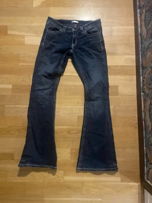 Blå bootcut jeans från Gina Tricot - Mörkblå jeans från Gina Tricot med tydliga vita sömmar och bootcut-modell. Klassisk femficksdesign och låg midja. Perfekta för dig som gillar en retroinspirerad look med utsvängda ben.