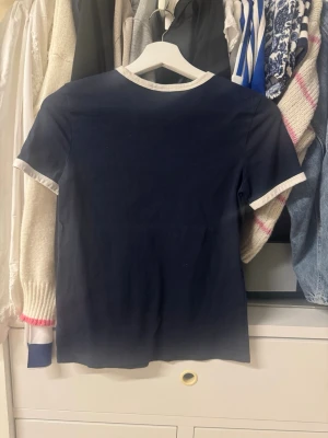 Mörkblå t-shirt med vita detaljer - En stilren mörkblå t-shirt med vita kanter vid ärmslut och halsringning. Klassisk passform och enkel design som passar till det mesta. Perfekt för dig som gillar en clean och tidlös look.