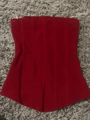 Röd topp - Korsett topp i röd  med figurnära passform och markerad midja. Axelbandslös design och lätt utsvängd nederkant ger en snygg siluett. Perfekt för att skapa en statement-look.