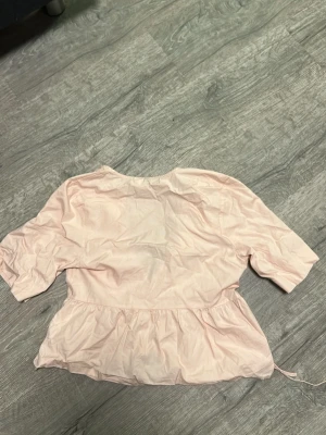 Ljusrosa blus från hm - Ljusrosa med volang med till. Mycket fin passform. Kan behövas stryka då den blir mycket finare! Även ett knyte på mitten. Skriv om ni vill se på!