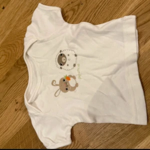 Vit t-shirt med djurtryck från H&M - Söt vit t-shirt från H&M i ekologisk bomull med korta ärmar. Framsidan har gulligt tryck med ett får och en kanin som håller en morot. Perfekt för dig som gillar mjuka och bekväma plagg med charmiga detaljer.