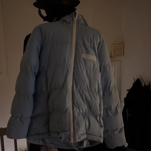 Ljusblå pufferjacka från Hoodrich - Säljer en ljusblå pufferjacka från Hoodrich med cool sned dragkedja och broderad logga på bröstet och ryggen. Jackan har huva, långa ärmar och ett band med H-loggor på insidan. 
