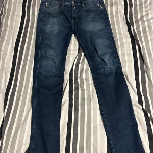Replay jeans - Snygga mörkblå jeans från Replay med klassisk femficksdesign och diskreta slitningar. Jeansen har smal passform och raka ben, perfekt för en stilren look. Tidlös modell med dragkedja och knapp i midjan.