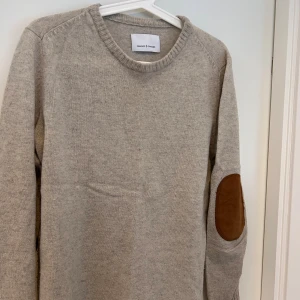 Beige stickad tröja Samsøe Samsøe - Snygg beige stickad tröja från Samsøe Samsøe med rund hals och bruna mockadetaljer på armbågarna. Perfekt för dig som gillar stilrena och klassiska plagg med en twist. Långärmad och mjuk, passar till jeans eller chinos.