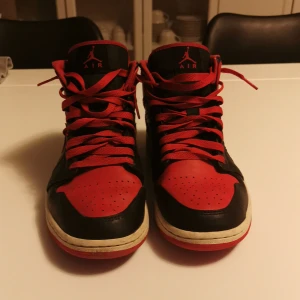Nike Air Jordan 1 svart/röd US9 - Säljer ett par Nike Air Jordan 1 i klassisk svart och röd färg. Skorna har högt skaft, snörning och den ikoniska Jumpman-loggan på plösen. Tillverkade i skinn med röda och svarta paneler samt vit mellansula. Perfekta för dig som vill sticka ut med en tidlös sneaker. Använda fåtal gånger, ny pris 1500kr